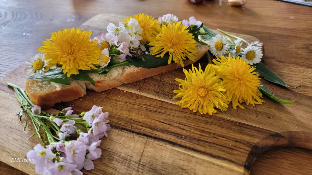 Brot mit Butter und essbaren Löwenzahn- und Wiesenschaumkrautblüten auf Holzbrett, im Kontext Ernährung und Natur in KiTa